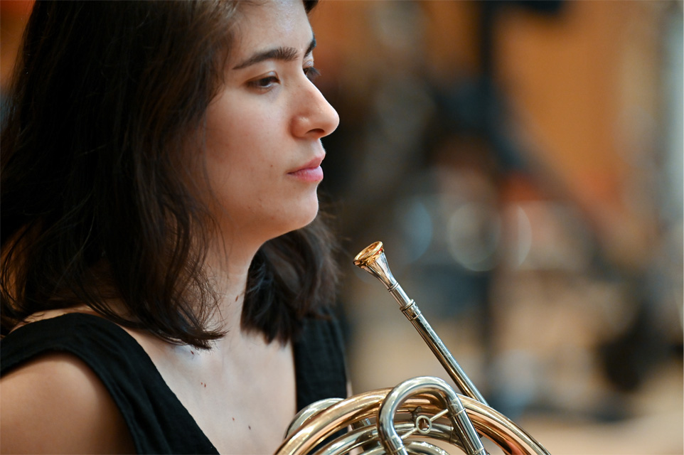 Close up of female student with dark hair, holding her French horn in a Wind orchestra.